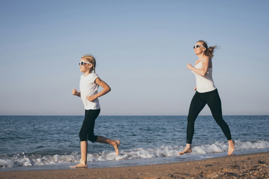 Mother and daughter running on the beach at the day time.